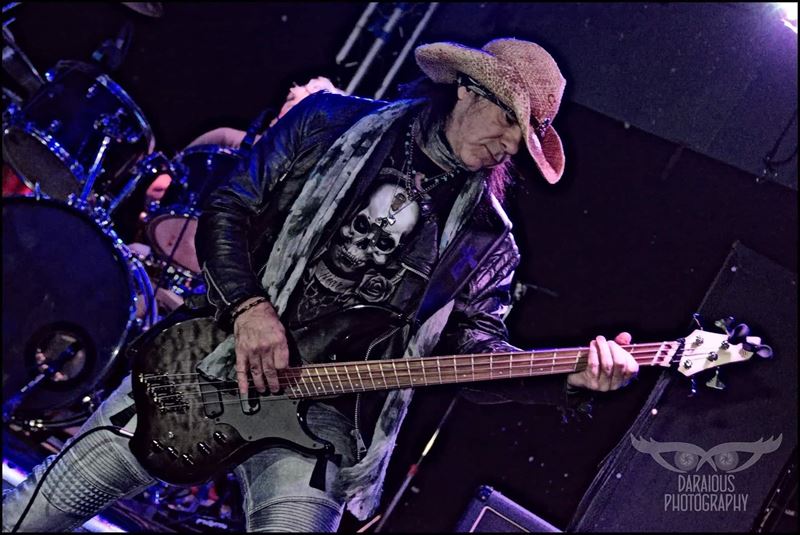 Bassist in a cowboy hat playing under purple stage lights
