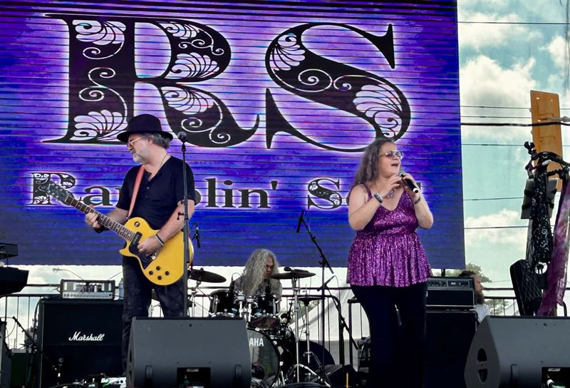 Guitarist and singer in purple sequins on stage in front of the Ramblin Soul' RS backdrop